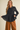 A woman modeling a black textured long-sleeve button-up blouse with a peplum waist, paired with wide-leg brown pants, against a solid beige background.