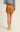 A person shown from the back wearing a mustard brown faux-suede mini skirt, a heather gray sweater, and pale yellow loafers, against a plain light beige studio background.