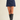 A model wearing a navy blue suede A-line mini skirt with a black lace waistband, paired with black leather knee-high boots, against a plain beige studio background.