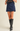 A model wearing a navy blue suede A-line mini skirt with a black lace waistband, paired with black leather knee-high boots, against a plain beige studio background.