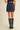 A model shown from the back wearing a navy blue mini skirt, a black lace-trimmed top, and black knee-high leather boots against a plain beige studio background.