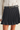 A black pleated mini skirt with a matching black belt featuring a gold buckle, styled with a white textured blouse.