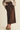 A person wearing a brown corduroy midi skirt with front patch pockets, styled with a beige ribbed knit sweater and brown flat shoes against a plain light beige studio background.