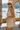 Woman in a beige outfit with sunglasses standing by a waterfront with stone architecture.