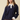 A woman modeling a navy blue knit sweater with a white collar and white button placket, layered over a brown mini skirt, against a solid beige background.
