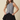 A woman modeling a sleeveless black and white gingham button-front top paired with a black pleated mini skirt, set against a solid beige background.