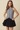 A woman modeling a sleeveless black and white gingham button-front top paired with a black pleated mini skirt, set against a solid beige background.