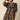 A woman wearing a navy blue tiered dress with a mustard yellow floral print, featuring puff sleeves and a ruffled neckline, posed against a solid beige background.