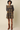 A woman modeling a navy blue mini dress with a gold floral pattern, puffed sleeves, and a smocked bodice, paired with brown leather cowboy boots against a solid beige background.