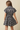 A woman shown from the back wearing a short-sleeve plaid dress with a button-up collar and flared skirt, photographed against a plain beige studio background.