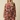 A woman modeling a brown long-sleeve mini dress with a pink and orange floral print, featuring a tie-waist belt and a ruffled skirt, set against a solid beige background.