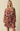 A woman modeling a brown long-sleeve mini dress with a pink and orange floral print, featuring a tie-waist belt and a ruffled skirt, set against a solid beige background.