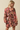 A woman shown from the back wearing a brown long-sleeve mini dress with a pink, orange, and cream floral print, paired with large gold hoop earrings, against a solid beige background.