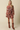 A woman modeling a long-sleeve brown floral mini dress with a drawstring waist, paired with brown leather cowboy boots, against a solid beige studio background.