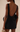 Woman wearing a black dress with an open back, holding a small handbag.