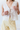 Person wearing a white lace top and light yellow pants against a plain background