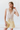 Woman wearing a white lace top and yellow shorts against a white background