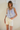 Woman wearing a light blue floral sleeveless top and white shorts against a plain background