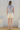 Woman wearing a sleeveless floral top and white shorts standing in a room with a white door.