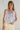 Woman wearing a light blue tie-dye sleeveless top and white pants against a plain background