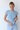Woman wearing a blue and white checkered shirt and light blue jeans against a white background