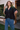 Woman wearing a black blouse and blue jeans standing outdoors.