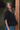 Woman wearing a black top and blue jeans standing indoors.