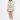 A model stands against a plain white studio background wearing a beige and white argyle knit cardigan and matching mini skirt set, paired with cream socks and brown loafers.