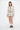 A model stands against a plain white studio background wearing a beige and white argyle knit cardigan and matching mini skirt set, paired with cream socks and brown loafers.
