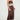 A woman models a brown satin maxi dress with white floral lace trim at the bust and hem, styled with brown heels against a plain light gray studio background.