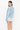 A woman modeling a light blue knit sweater and light denim shorts with cream lace trim, photographed against a plain white studio background.