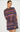 A woman modeling a chunky knit sweater dress with horizontal stripes in purple, blue, pink, and orange on a light gray background.