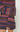 A close-up of a person wearing a chunky knit sweater with horizontal multicolor stripes in pink, purple, blue, and orange-brown tones, cropped from the chest down against a plain light background.