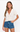 Woman wearing a white crochet top and denim shorts on a white background