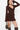 A woman modeling a dark brown long-sleeve mini dress with ruffle details, paired with dark brown suede boots and holding a matching brown handbag, against a plain white background.