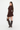 A woman modeling a dark brown ruffled long-sleeve mini dress with textured knit detailing, paired with dark brown knee-high boots and a matching brown handbag, against a plain white studio background.