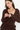 A woman wearing a dark brown textured knit long-sleeve top with ruffle details, shown from the chest down against a plain white background.