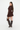 A woman modeling a dark brown ruffled long-sleeve mini dress with side cutouts, paired with dark brown knee-high boots and a matching handbag, against a plain white studio background.