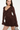 A woman wearing a dark brown long-sleeve mini dress with ruffle details, photographed against a plain white studio background.