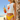 Woman in yellow bikini and white crop top with red design holding a cocktail on a beach.