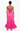 A woman viewed from the back wearing a bright pink satin-like strap dress with a ruched bodice and a ruffled hem, paired with pink heels against a plain white studio background.