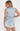 A woman modeling a light blue satin two-piece pajama set with white lace trim, shown from the back against a plain white background.