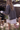 A woman from behind wearing a dark gray oversized knit cardigan over a white dress, standing in an outdoor patio setting with wooden pergola beams and warm natural light.