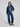 A model stands against a light gray studio background wearing a dark blue cropped denim jacket and matching wide-leg denim jeans over a light blue collared shirt, with brown suede loafers.