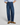 A person wearing dark blue wide-leg denim jeans, a light blue striped button-up shirt, and brown suede loafers, standing against a light gray studio background.