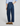 Rear view of a person wearing dark blue wide-leg denim jeans, a light blue and white striped shirt, and brown suede loafers against a light gray studio background.