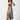 A woman modeling a sleeveless maxi dress with a zebra print pattern in beige, brown, and black, paired with brown cowboy boots, against a plain white studio background.