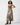 A woman modeling a sleeveless maxi dress with a zebra print pattern in beige, brown, and black, paired with brown cowboy boots, against a plain white studio background.