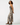 A woman modeling a sleeveless maxi dress with a zebra print pattern in beige and black, paired with brown leather cowboy boots, against a plain white studio background.