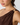 Close-up of a model wearing a dark brown one-shoulder draped top with a wide gold metal ring detail at the shoulder, against a light gray background.